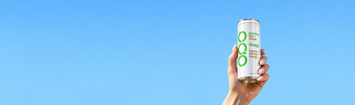 A hand holding a white can of Ooho! Energy Drink against a bright blue sky background.